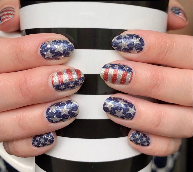 May include: Close-up of hands with red, white and blue glitter nail polish. The nails are decorated with stars and stripes.