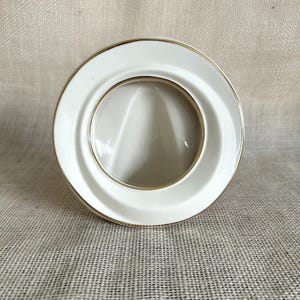 May include: A white ceramic picture frame with a gold trim. The frame has a circular opening for a photo.