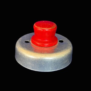 May include: A vintage metal biscuit cutter with a bright red wooden handle. The cutter has a circular shape with a slightly worn, silver-colored finish. Two small holes are visible on the metal rim.