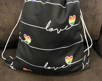 May include: Black drawstring bag with white stripes and rainbow hearts. The bag has the word "love" written on it.