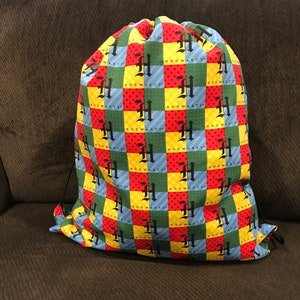 May include: A drawstring bag with a Hogwarts theme. The bag is made of a colorful fabric with a checkered pattern in red, yellow, green, and blue. The pattern features the Hogwarts crest and the words "Hogwarts" repeated throughout.