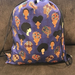 May include: A purple drawstring bag with a pattern of black and brown stylized female faces. The faces are wearing colorful head wraps.