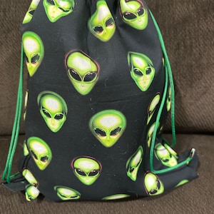 May include: A black drawstring bag with a green alien face pattern. The bag has green drawstrings.