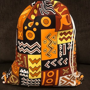 May include: A drawstring bag with a colorful African print design. The bag is made of fabric and has a white drawstring. The print features geometric shapes, zigzags, and circles in shades of orange, yellow, brown, and black.