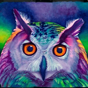 May include: A close-up of a colorful watercolor painting of an owl. The owl's eyes are bright orange, and its feathers are a mix of purple, blue, green, and yellow.