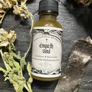 May include: A glass bottle with a dropper filled with a yellow liquid. The label reads "Handfuls of Dust Apothecary Empath Soul Grounding & Nurturing Oil Blend for the Empathic Soul".