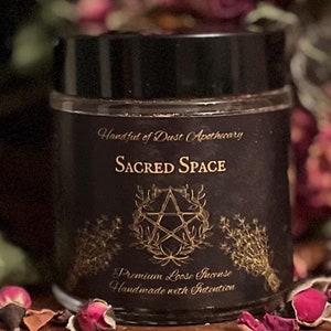 May include: A black jar with a gold label that reads "Handful of Dust Apothecary" and "Sacred Space" with a pentagram symbol. The label also says "Premium Loose Incense" and "Handmade with Intention". The jar is sitting on a wooden surface with dried rose petals.