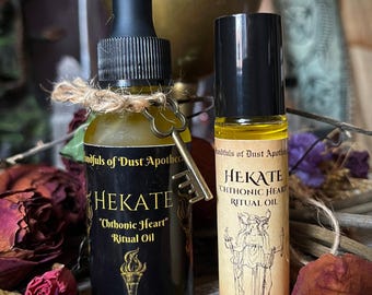 Może przedstawiać: Dwie butelki olejku rytualnego. Jedna to ciemna szklana butelka z zakraplaczem, zawieszką w kształcie klucza i napisem "HEKATE 'Chthonic Heart' Ritual Oil". Druga to butelka roll-on z napisem "HEKATE CHTHONIC HEART RITUAL OIL" i ilustracją.