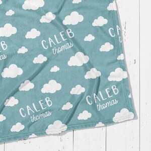 May include: A light blue blanket with a white cloud pattern and the name "CALEB Thomas" printed in white. The blanket is made of a soft material and is suitable for a baby or child.