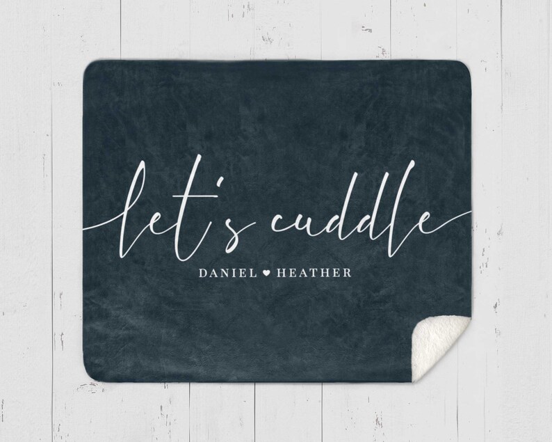 Puede incluir: Una manta de forro polar azul oscuro con el texto "let's cuddle" en escritura cursiva blanca. Debajo del texto, dice "DANIEL &hearts; HEATHER".