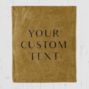 Puede incluir: Una manta de microfibra amarilla mostaza con el texto "YOUR CUSTOM TEXT" impreso en negro.