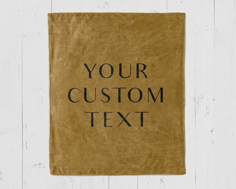 Puede incluir: Una manta de microfibra amarilla mostaza con el texto "YOUR CUSTOM TEXT" impreso en negro.