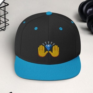 Pu&ograve; includere: Cappellino da baseball nero e blu con visiera piatta. Il cappellino presenta un disegno ricamato di due mani gialle che sorreggono un diamante blu. Il bottone superiore e gli occhielli sono blu.