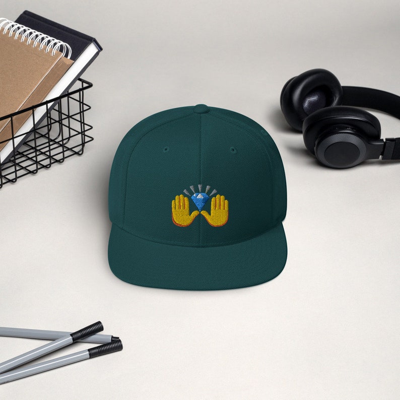 Pu&ograve; includere: Cappellino da baseball verde scuro con visiera piatta. Il cappellino presenta un disegno ricamato di due mani gialle che sorreggono un diamante blu con luce radiante. Il cappello &egrave; uno stile classico, adatto per l'uso casuale.