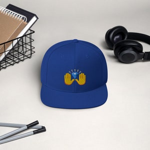 Pu&ograve; includere: Cappellino da baseball blu reale con visiera piatta. Il cappellino presenta un disegno ricamato di mani gialle che sorreggono un diamante blu con linee radianti. Il cappello &egrave; uno stile classico, adatto all'abbigliamento casual.