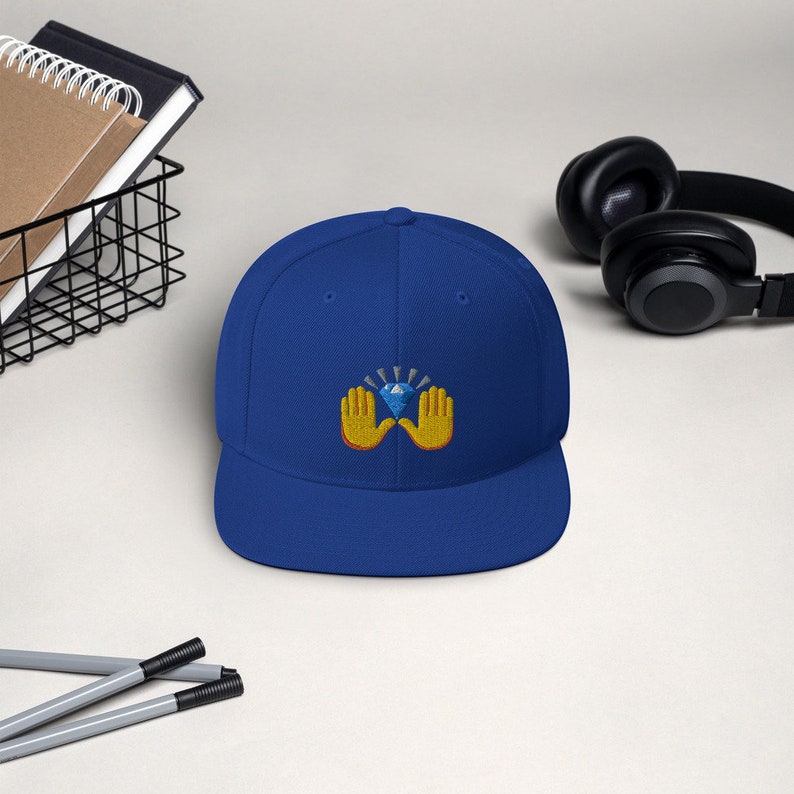 Pu&ograve; includere: Cappellino da baseball blu reale con visiera piatta. Il cappellino presenta un disegno ricamato di mani gialle che sorreggono un diamante blu con linee radianti. Il cappello &egrave; uno stile classico, adatto all'abbigliamento casual.