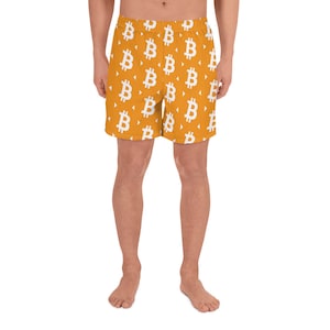 May include: Orange athletic shorts with a repeating white Bitcoin symbol pattern. The shorts are knee-length and made of a lightweight material, suitable for sports or casual wear.