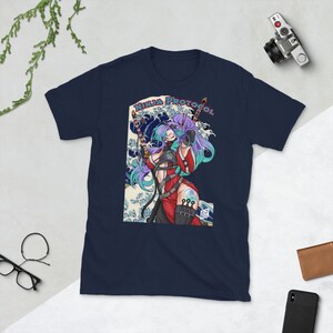 Op de afbeelding: Marineblauw t-shirt met een afbeelding van een vrouwelijke ninja met paars en blauwgroen haar, die twee zwaarden vasthoudt. Het ontwerp bevat de tekst "NINJA PROTOCOL" en een golfpatroon achtergrond.