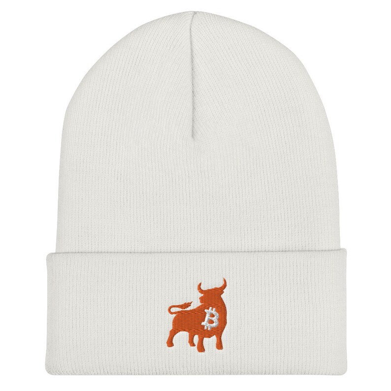 May include: A white beanie featuring an embroidered orange bull with a Bitcoin symbol. The beanie is made of a soft, knitted material and has a folded cuff. The bull graphic is located on the lower front of the hat.