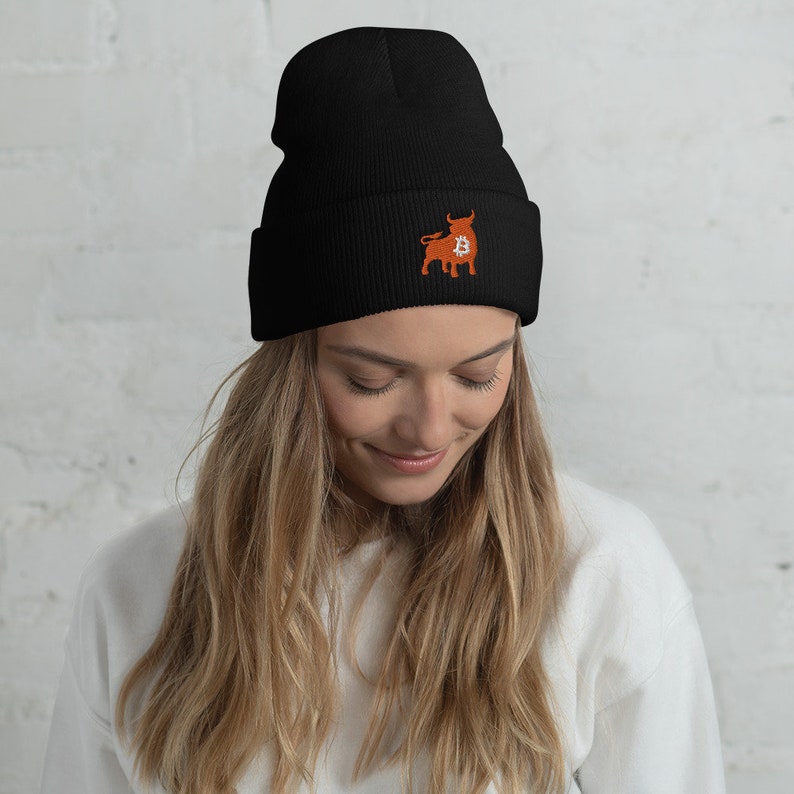 May include: Black beanie with an embroidered orange bull logo featuring a Bitcoin symbol. The beanie is made of a soft, knitted material. The hat is a stylish accessory for cryptocurrency enthusiasts.
