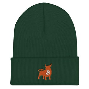 May include: A dark green beanie with a folded brim. An orange bull graphic with a Bitcoin symbol is embroidered on the front. The beanie is made of a soft, knitted material.