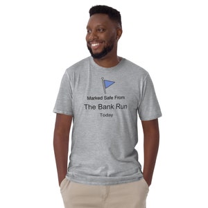 Puede incluir: Camiseta gris claro con el texto "Marked Safe From The Bank Run Today" y un gráfico de bandera azul. La camiseta es de material suave y tiene mangas cortas.