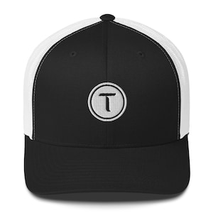 May include: Black and white trucker hat with a curved brim. The front panel is black with a white embroidered circular logo containing the letter "T". The back of the hat features white mesh for breathability.