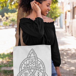 May include: White tote bag with a black graphic design featuring a triangle with text and symbols. The text includes phrases like "Speak with Love," "Know Your Power," and "Blessed Be." The bag is carried over the shoulder.