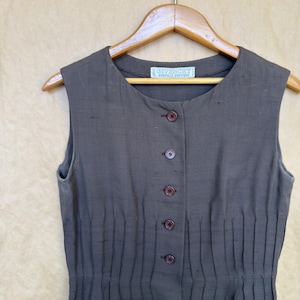 Pode incluir: Um vestido sem mangas, abotoado, na cor castanho escuro, pendurado num cabide de madeira. O vestido apresenta pregas verticais e uma pequena etiqueta na gola com o texto "GIVENCHY".