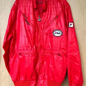 May include: Bright red vintage Fila jacket with a full zipper, multiple pockets, and a ribbed hem and cuffs. Features the Fila logo on the chest and sleeve. The jacket has a shiny, quilted appearance.