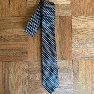 May include: A dark gray tie with a white grid pattern. The tie is lying on a wooden surface. The tie is a classic accessory for formal or business attire.