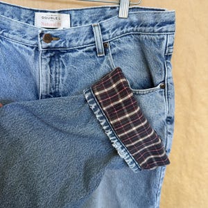 Op de afbeelding: Lichtblauwe spijkerbroek met een geruit manchet detail. De jeans heeft een knoopsluiting en een klassiek ontwerp met vijf zakken. Het label luidt "L.L.Bean Double L Natural Fit". De jeans hangt aan een houten kleerhanger.