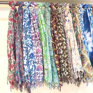 May include: A collection of colorful scarves with floral patterns hanging on a rack. The scarves are made of soft fabric and have fringed edges.