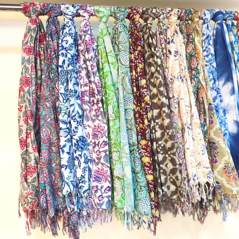 May include: A collection of colorful scarves with floral patterns hanging on a rack. The scarves are made of soft fabric and have fringed edges.