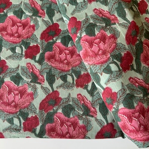 May include: A green fabric with a pink floral print. The fabric is folded in half and the floral pattern is visible on both sides.