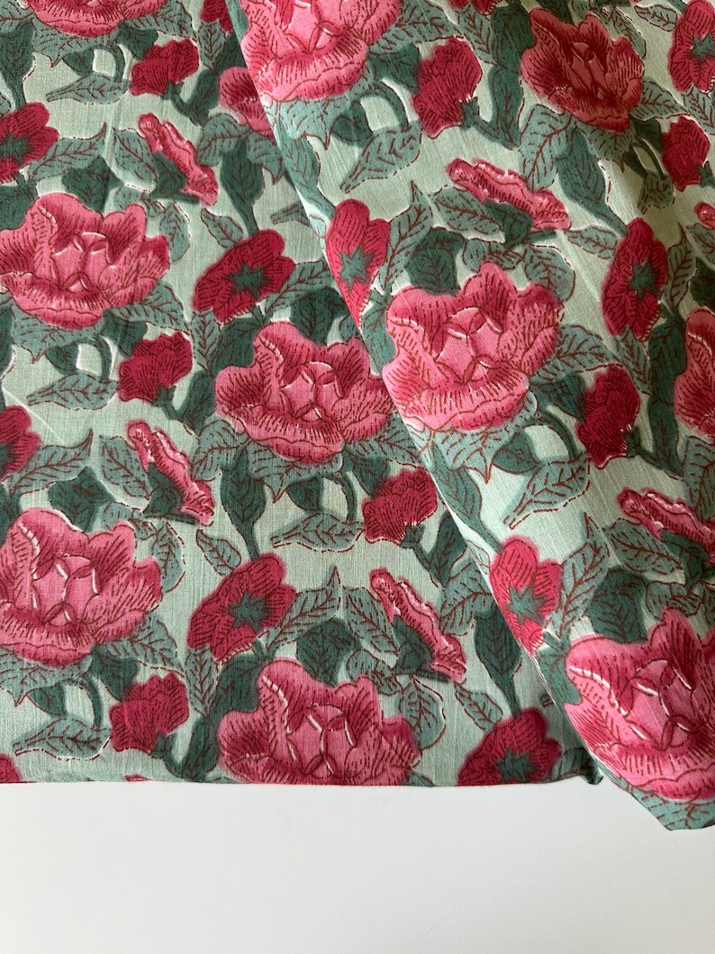 May include: A green fabric with a pink floral print. The fabric is folded in half and the floral pattern is visible on both sides.