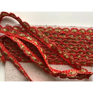 May include: Red and gold trim with a scalloped edge. The trim is made of a woven fabric with a delicate pattern.