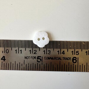 K&ouml;nnte beinhalten: Ein wei&szlig;er Plastikknopf mit Blumenmuster. Der Knopf hat einen Durchmesser von etwa 3,2 cm.