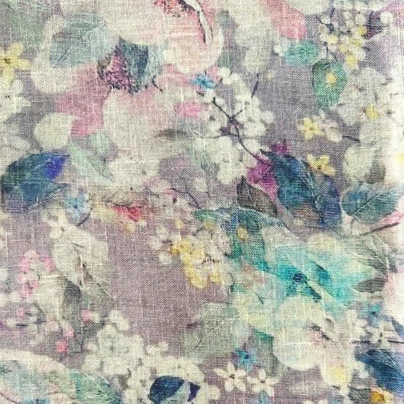 May include: Close-up of a floral fabric with a linen texture. The design features a mix of pastel colors, including pink, blue, yellow, and white, creating a soft, watercolor effect. The pattern includes flowers and leaves.