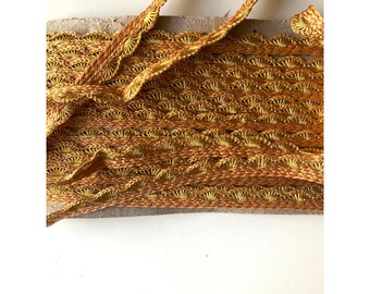 May include: A close-up of a gold and brown crocheted trim with a scalloped edge. The trim is made of a fine, delicate thread and has a subtle sheen.