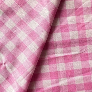 Könnte beinhalten: Rosa-weißes Gingham-Gewebe mit einem karierten Muster. Der Stoff ist in der Mitte gefaltet und zeigt das Muster auf beiden Seiten.
