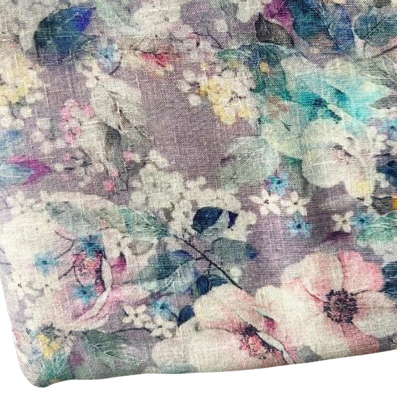 May include: Floral fabric with a watercolor effect. The design features large, light pink and white flowers, with accents of blue, green, and purple. The background is a muted lavender color, creating a soft and delicate aesthetic.