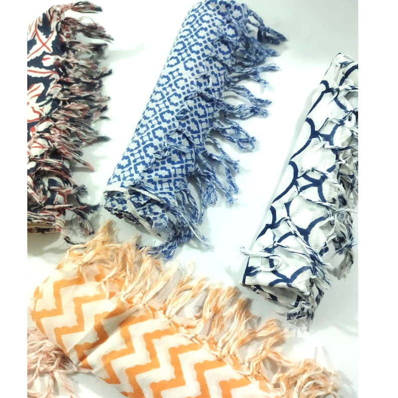 May include: Three cotton scarves with fringe edges. The scarves are folded and feature different geometric patterns in blue and white, and orange and white.