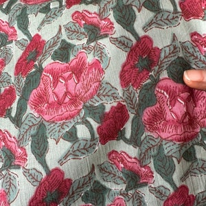 May include: A close-up of a fabric with a floral print. The fabric is a light green color with pink flowers and dark green leaves.