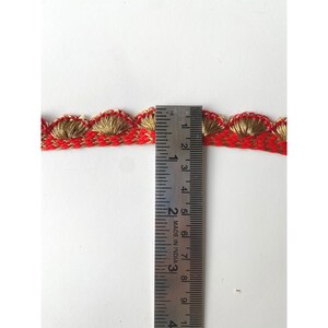 May include: Red and gold trim with a scalloped edge, measured with a ruler showing 2 inches in length.