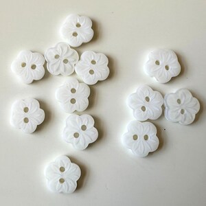 K&ouml;nnte beinhalten: Eine Sammlung von 12 wei&szlig;en, zweil&ouml;chrigen, blumenf&ouml;rmigen Kn&ouml;pfen. Die Kn&ouml;pfe haben ein erhabenes, strukturiertes Design.