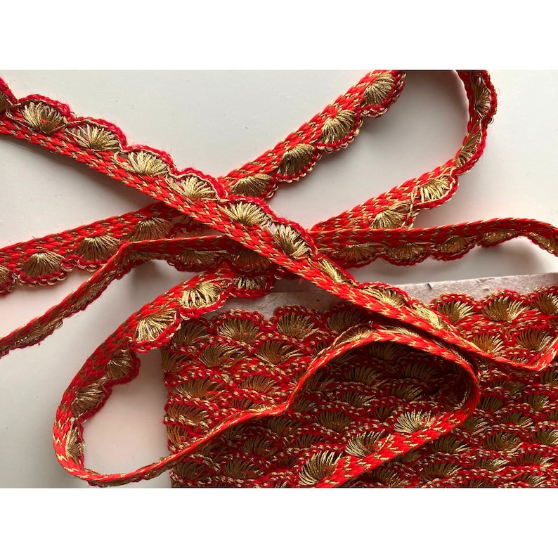 May include: Red and gold trim with a scalloped edge. The trim has a repeating pattern of small, gold, fan-shaped designs.