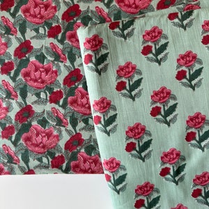 May include: Two pieces of fabric with a floral print. The top fabric is white with pink flowers and green leaves. The bottom fabric is light green with pink flowers and dark green leaves.