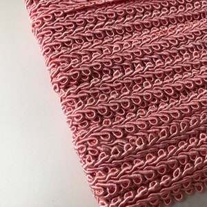 May include: Pink braided trim with a decorative looped pattern. This trim is perfect for adding a touch of elegance to any project.