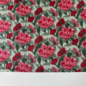 May include: A green fabric with a pink floral pattern. The fabric is covered in a repeating pattern of pink flowers with green leaves.